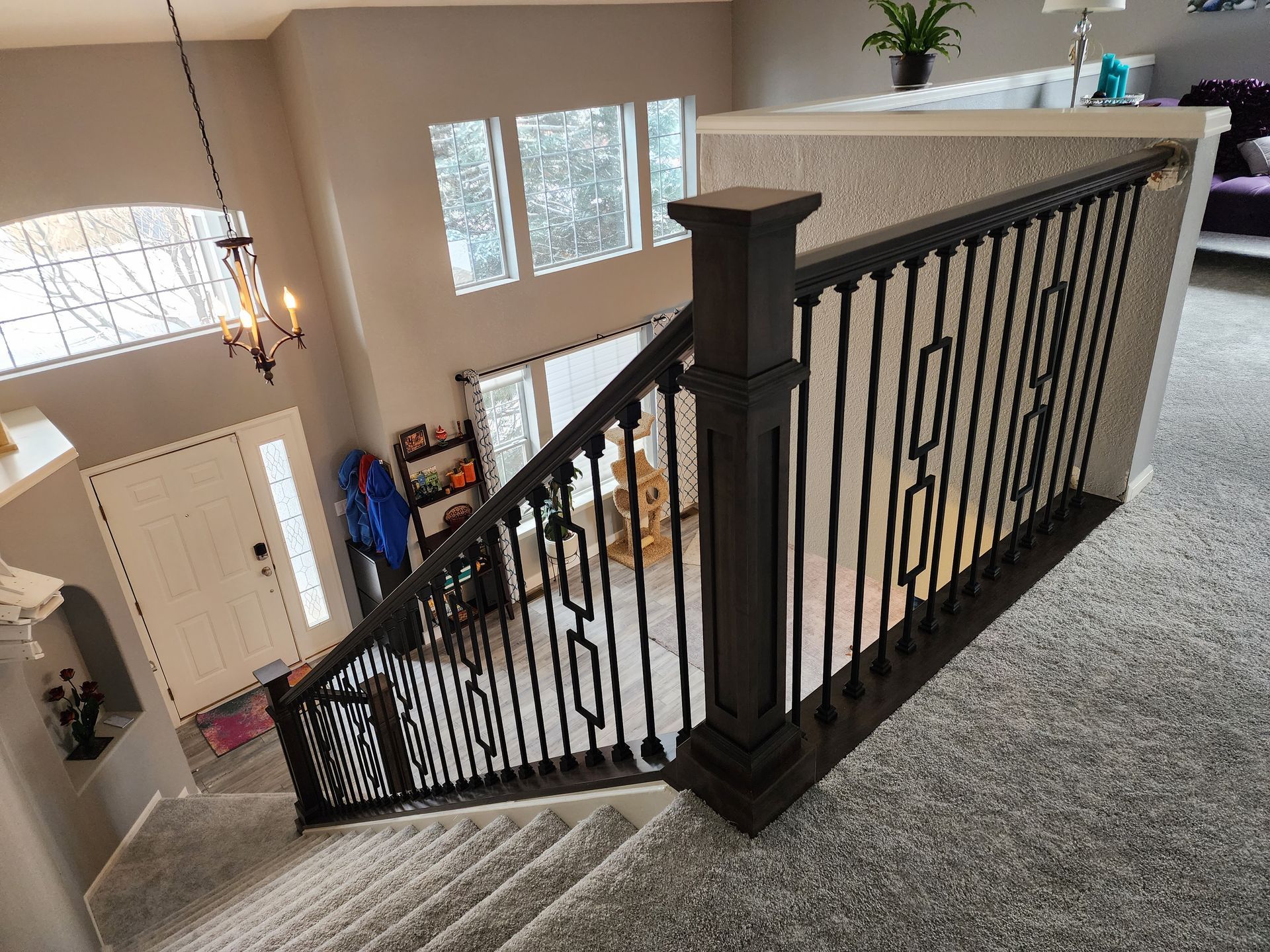 Staircase with black railing and gray carpet. View from above, overlooking the entry and front door.
