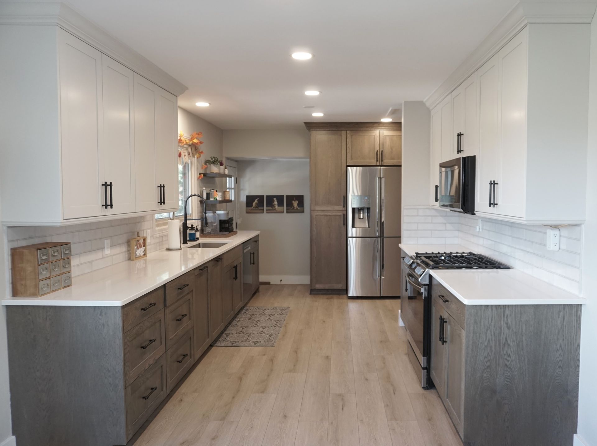 Modern kitchen with light wood floor, white and gray cabinets, and stainless steel appliances.