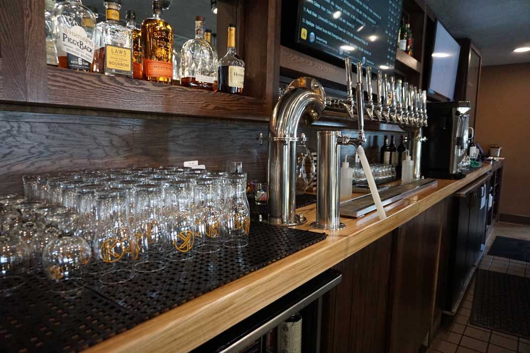 Bar interior with glasses, taps, and bottles, set against wood paneling and a TV.