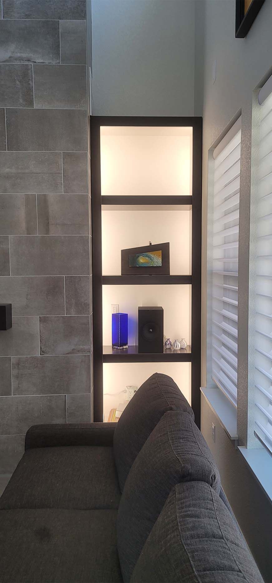 Built-in illuminated shelves with decorative objects next to a sofa and stone-tiled wall.