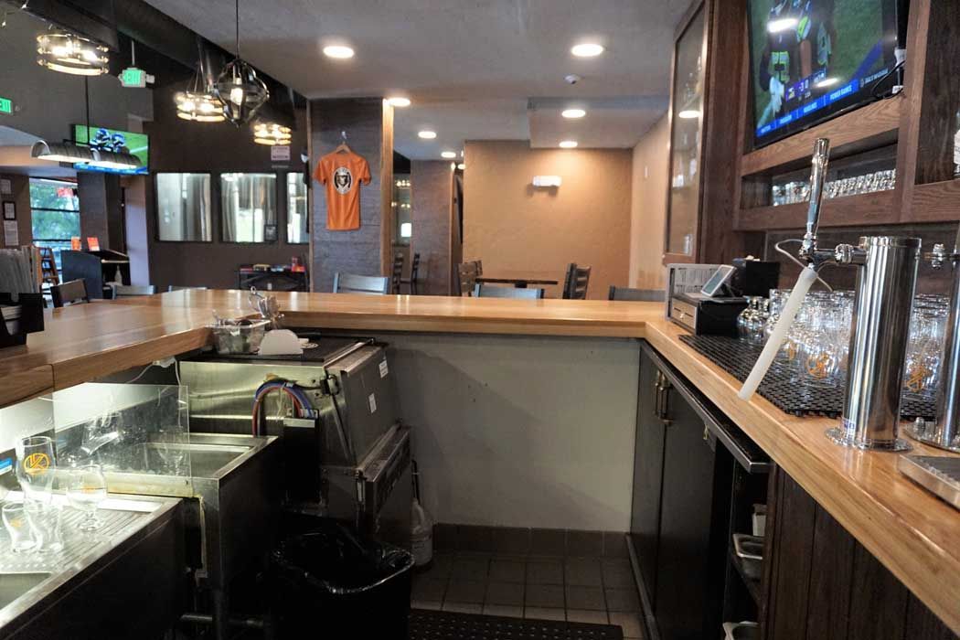 Interior bar view with wooden bar, stainless steel sinks, and a few tables.