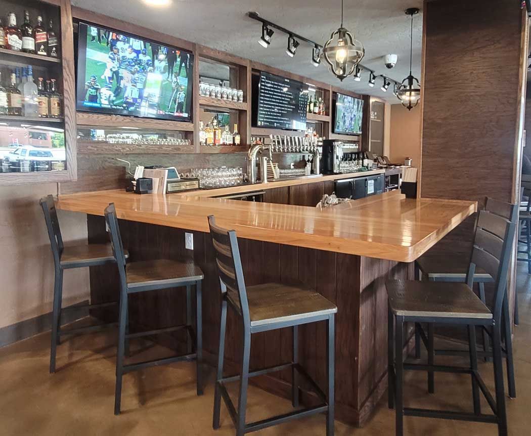 A bar with wooden countertop, bar stools, and televisions showing sports.