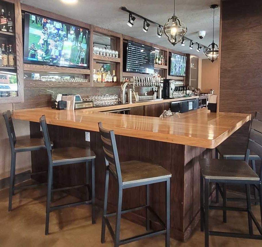 A bar with a long wooden counter and chairs in a restaurant.