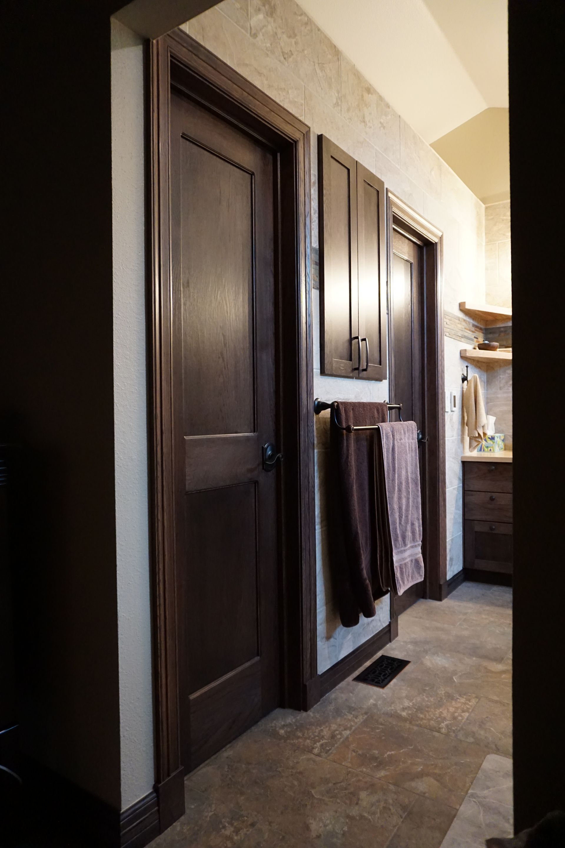 Dark wood doors and cabinets in a hallway with textured wall. Towels hang on a rack.