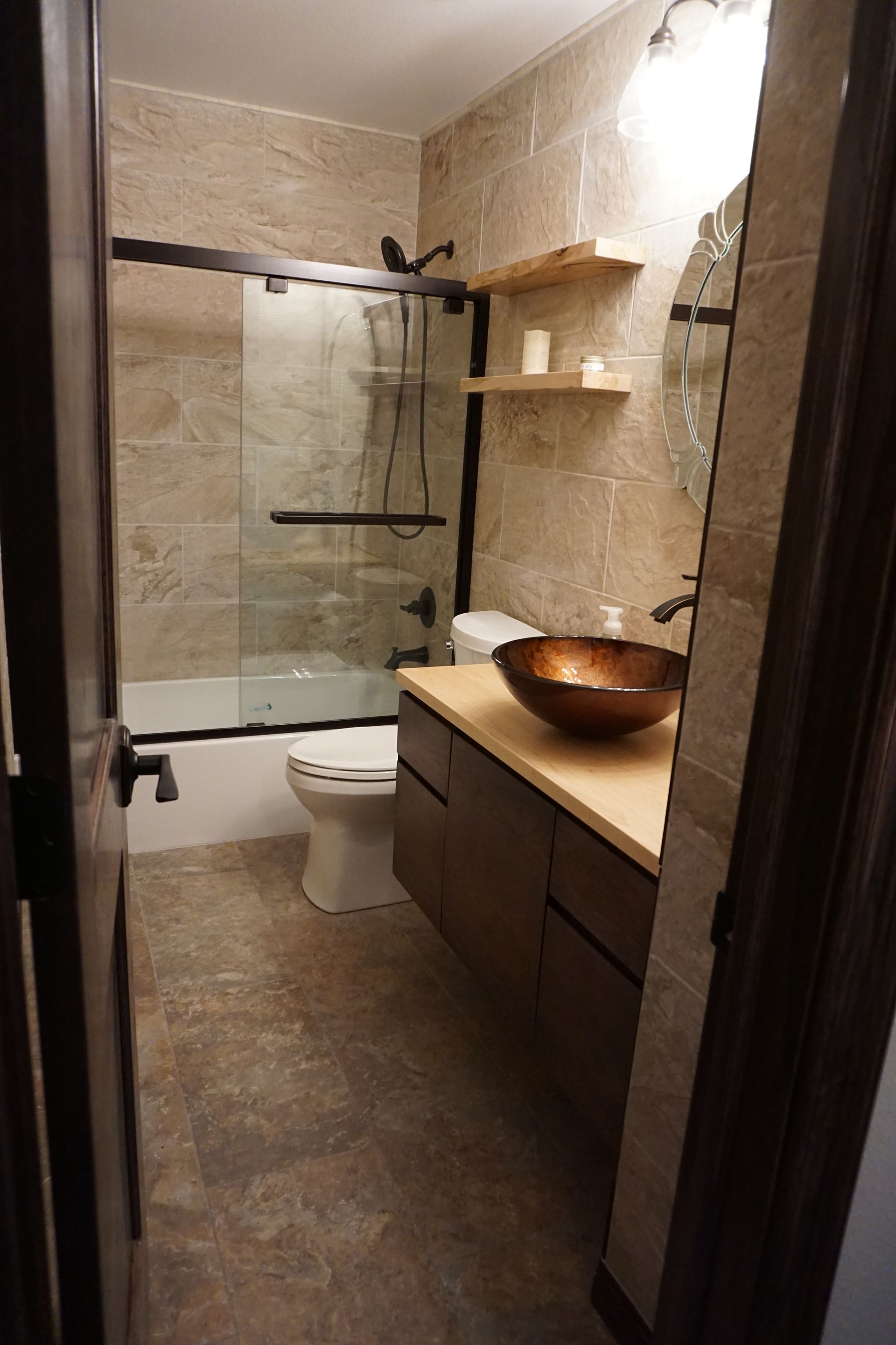 Bathroom with tan tile, dark wood vanity and shelves, and bronze sink bowl.