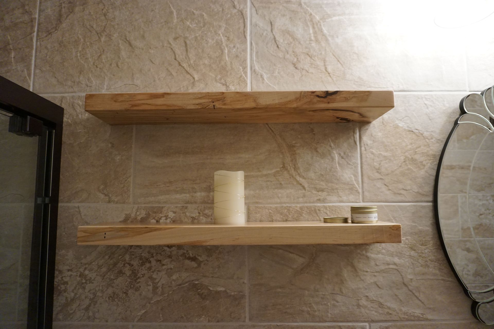 Two wooden shelves mounted on a tiled wall, holding a candle and small containers.