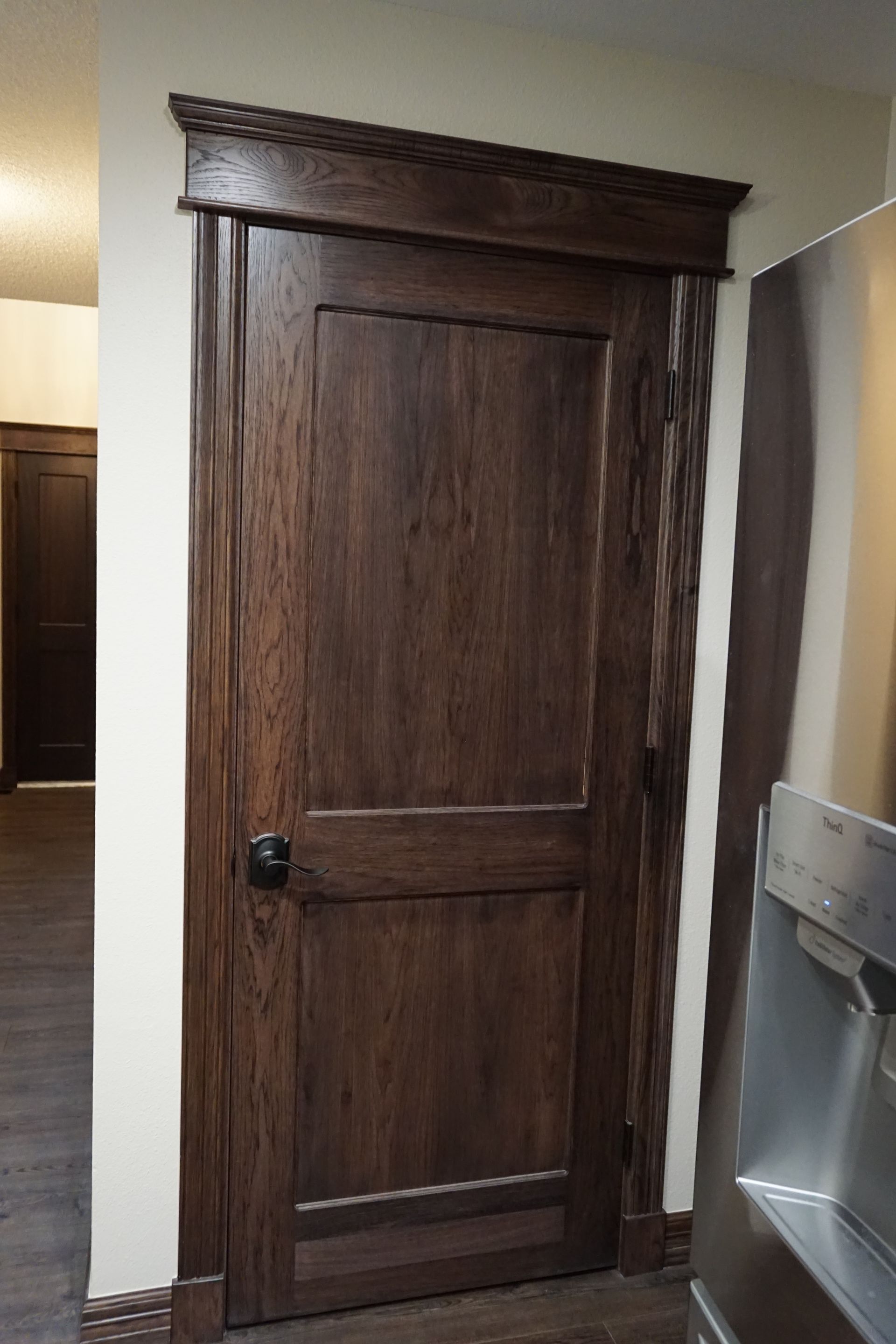 Dark wooden door with matching trim and black knob. Next to a silver refrigerator.
