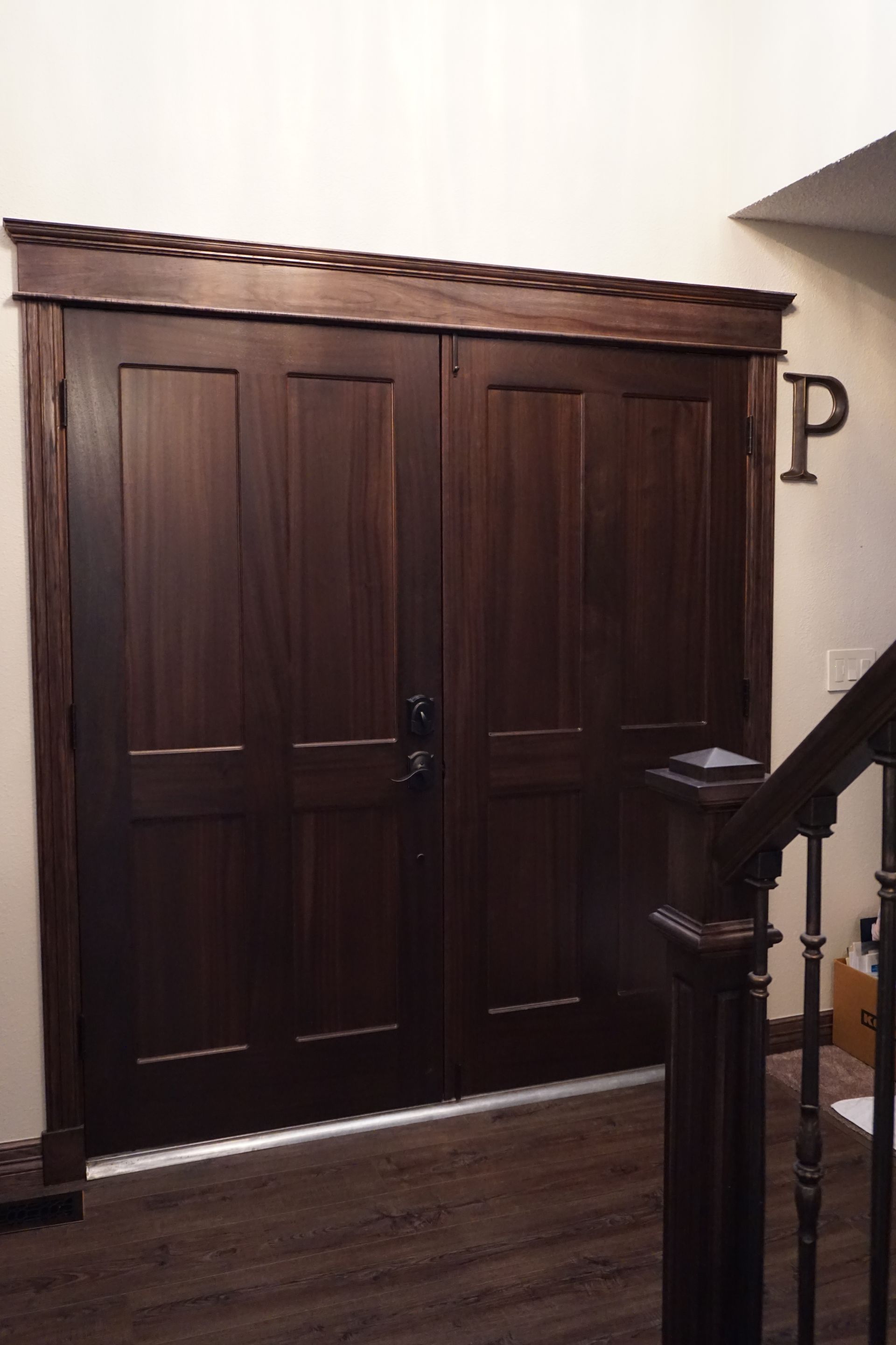 Dark wood double doors with ornate trim, leading to an interior. A staircase and letter 