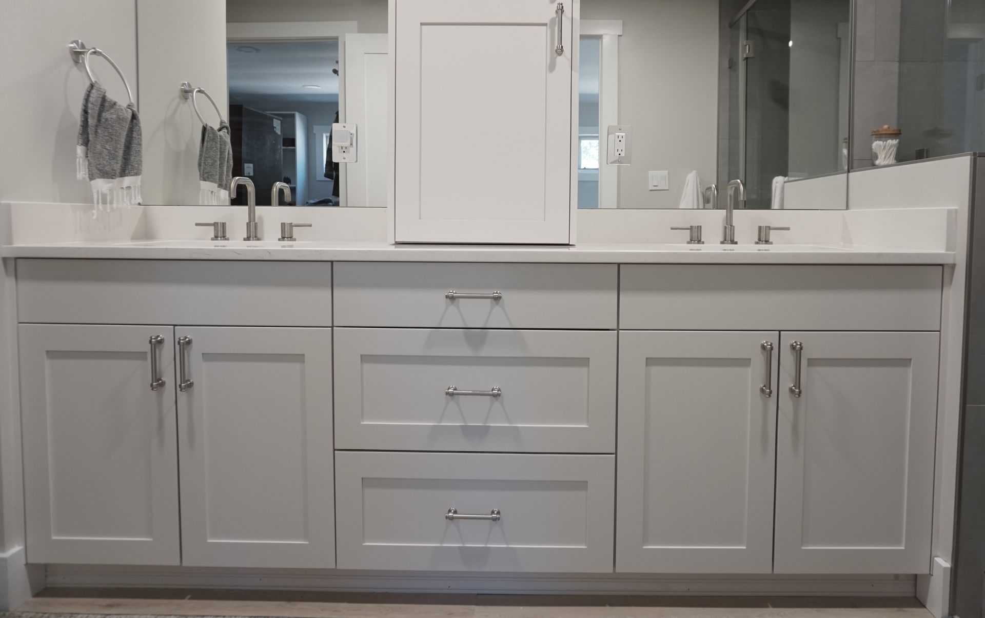 Gray bathroom vanity with double sinks, mirrors, and a central cabinet.