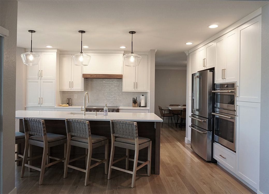 Modern kitchen with island, white cabinets, stainless steel appliances, and wood flooring.