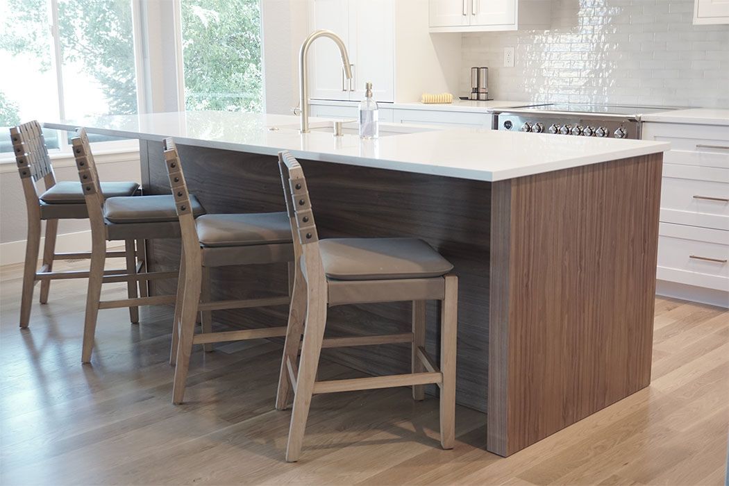 Kitchen island with a marble countertop, three bar stools, and a stainless steel faucet.