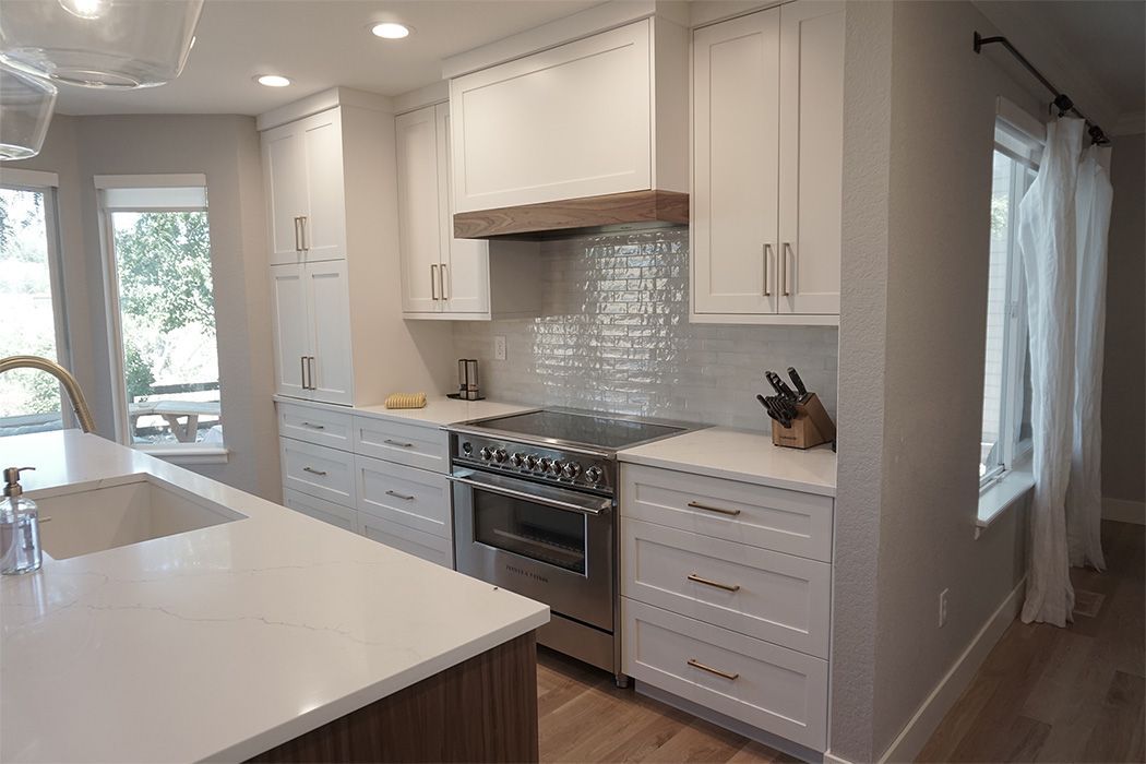 White kitchen with stainless steel appliances, wood accents, and window with sheer curtains.