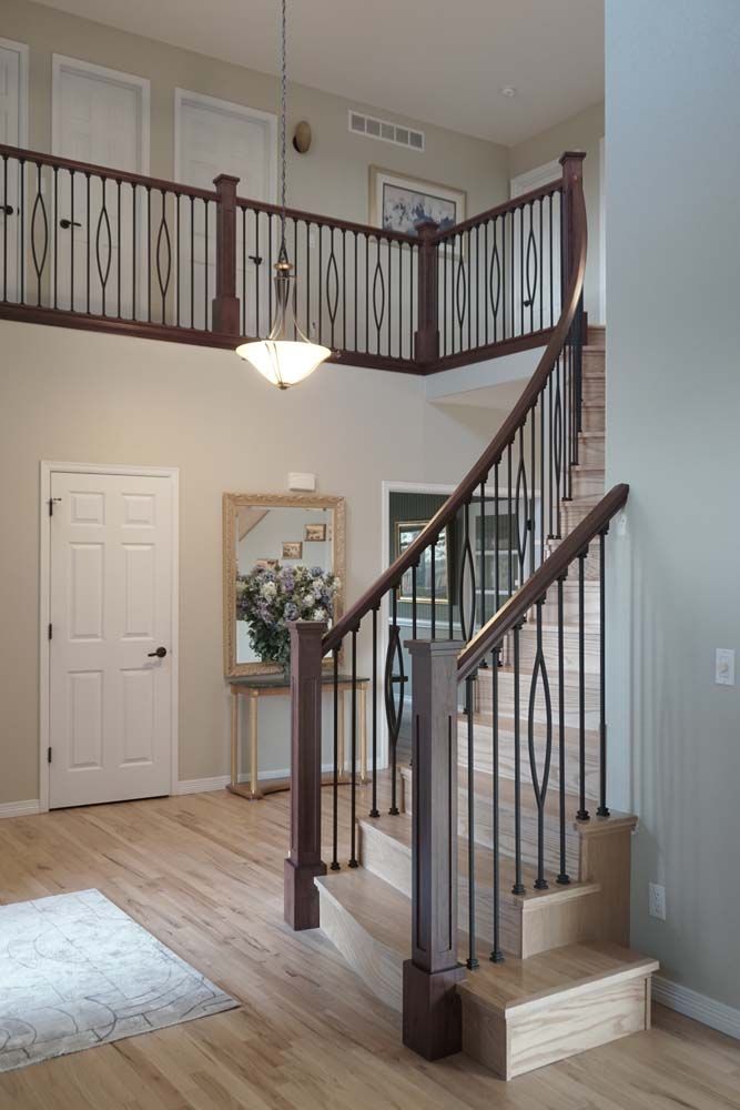 Wooden staircase in a home's entryway, with a second-story landing, ornate dark metal railing, and light-colored walls.