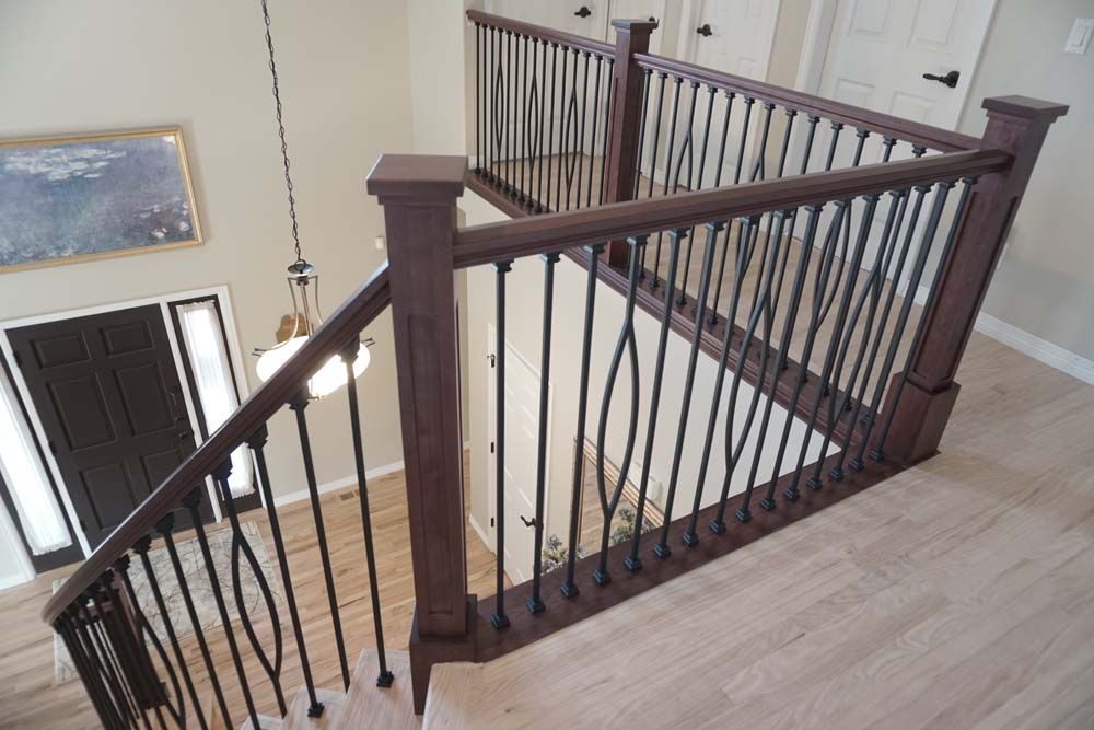 Staircase with dark wood railing and black iron balusters, light wood floor and trim.