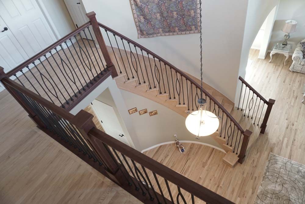High-angle view of a wooden staircase with black metal balusters. Bright lighting, light-colored walls and flooring.