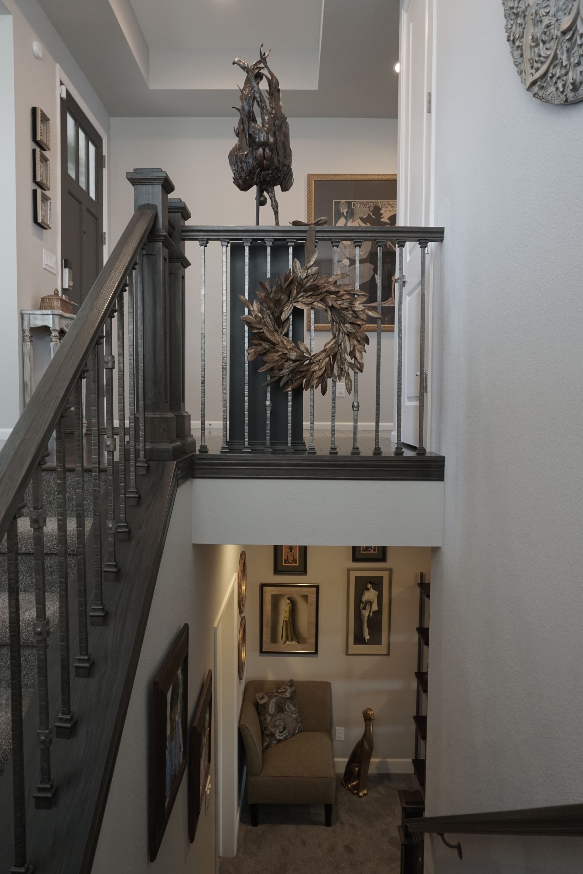 Staircase with dark gray railing and steps, leading to a landing with a horse statue and wreath; a hallway below.