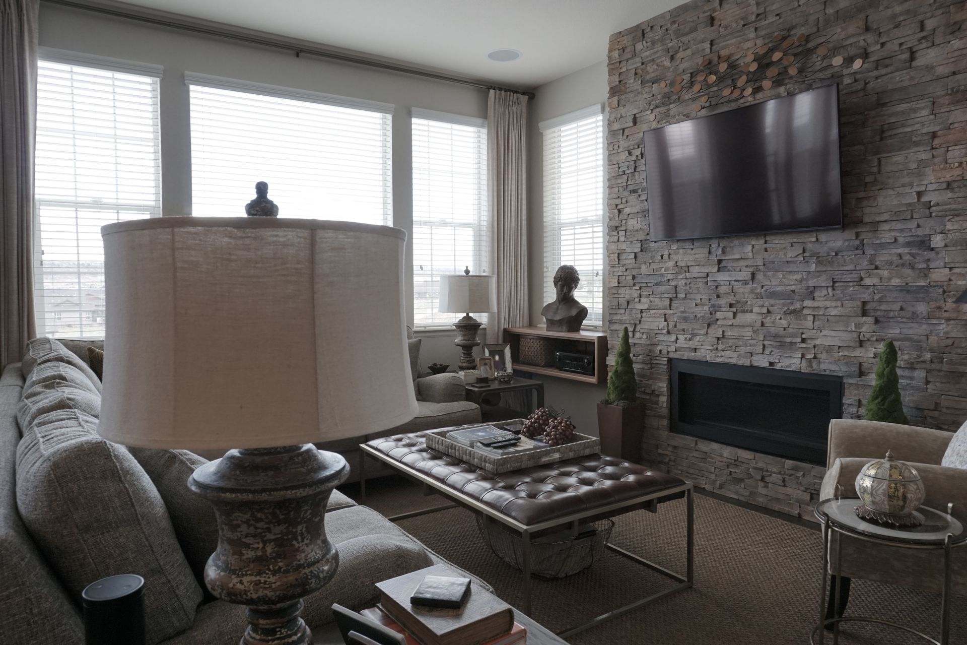 Cozy living room with stone fireplace, TV, and large windows.  Neutral colors and modern furniture create a warm ambiance.