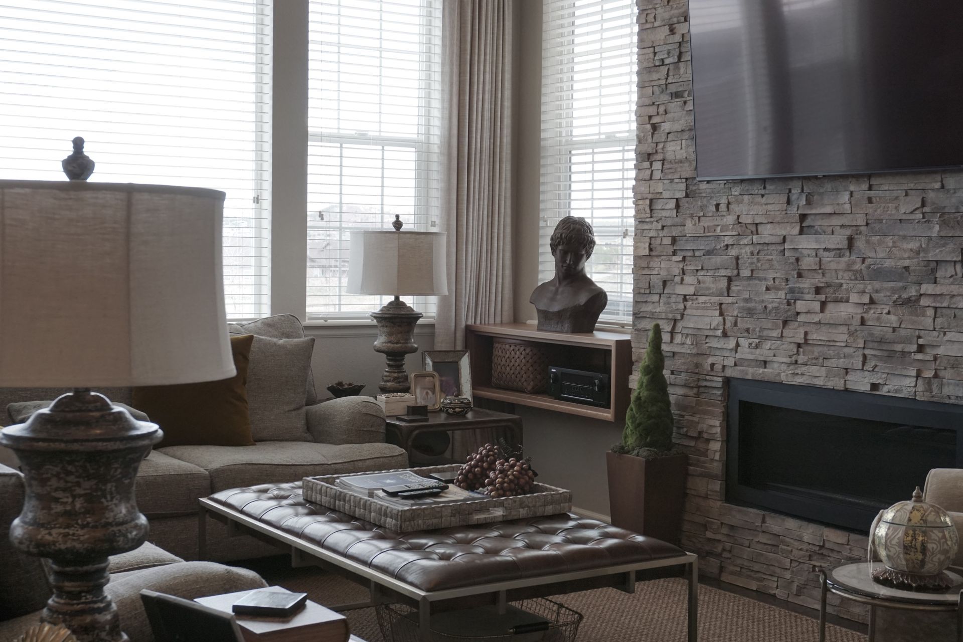 Living room with stone fireplace, windows, sectional sofa, and tufted ottoman.