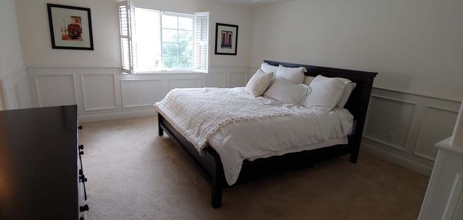 Bedroom with white walls, a dark bed frame, and light bedding. Two framed pictures hang on walls.