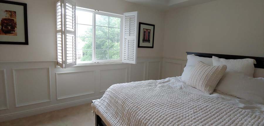 Bedroom with white walls, window, shutters, and bed with white bedding.