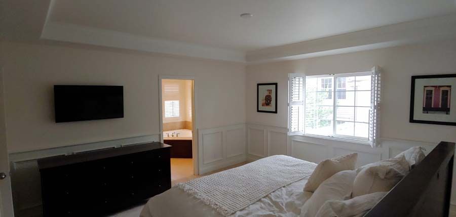 Bedroom with bed, television, and bathroom door. White walls, window, and black dresser.