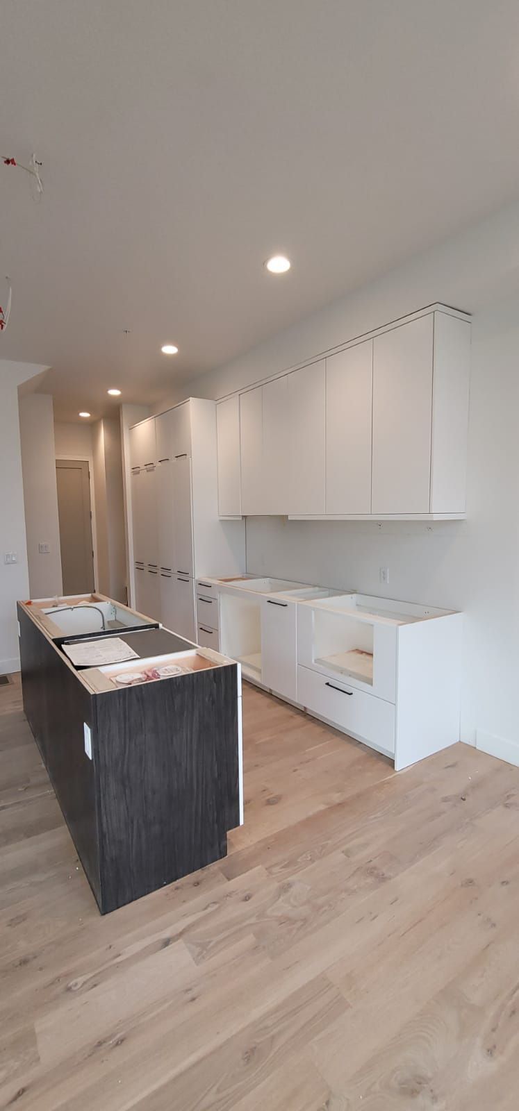 Kitchen with white cabinets, dark island, light wood floor, and recessed lighting.