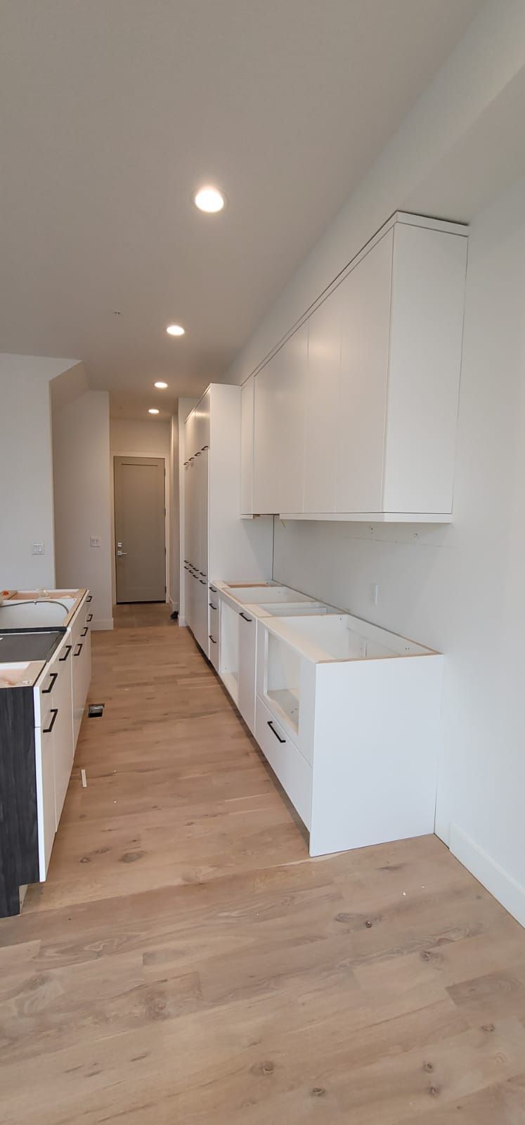 Kitchen with white cabinets under construction, light wood floors, recessed lighting.