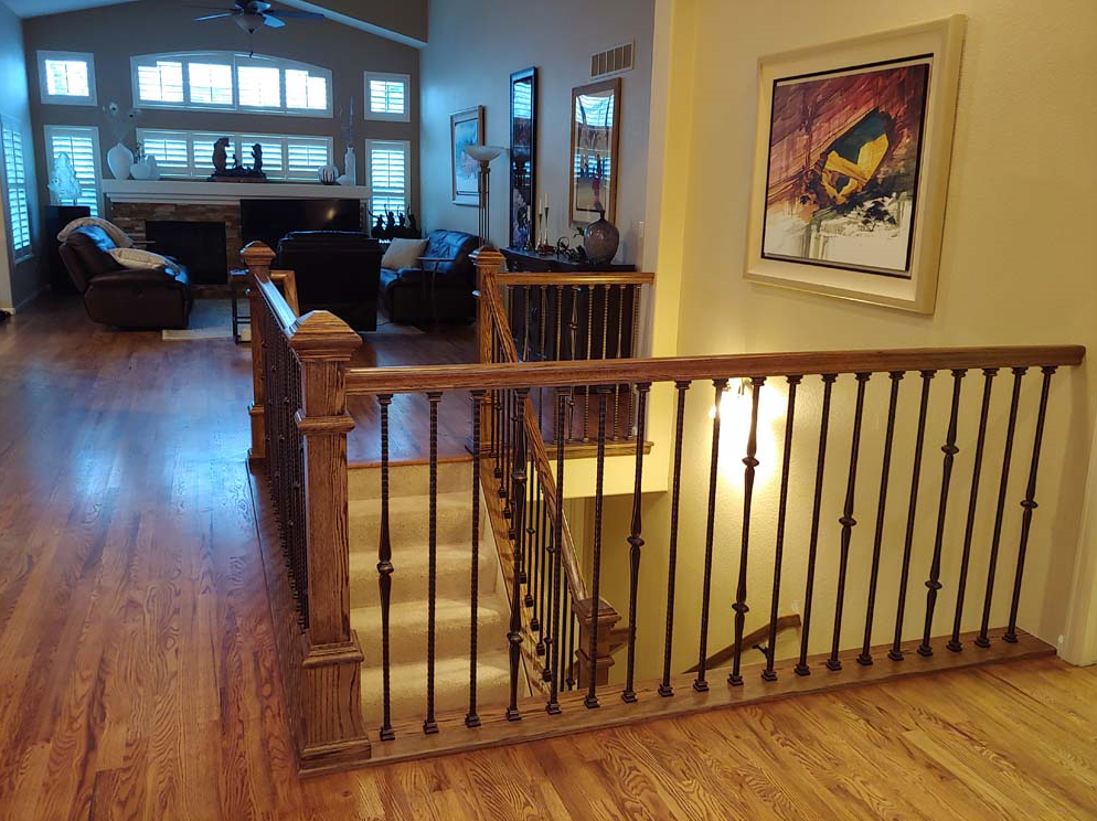Wooden staircase with ornate black spindles, leading down to a lower level. Warm wood flooring throughout.