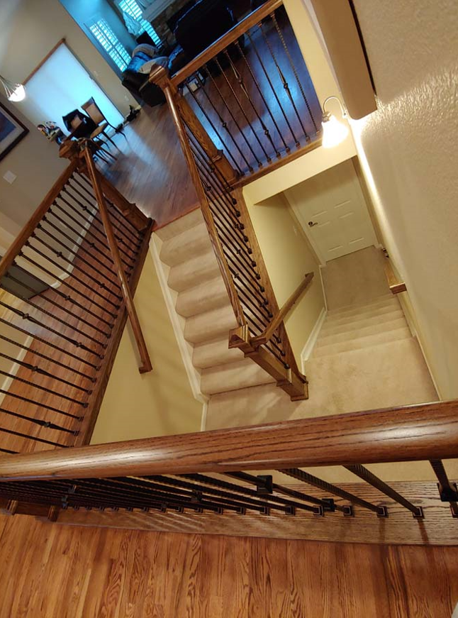 Overhead view of a home's staircase with wood railings, iron balusters, and carpeted steps.