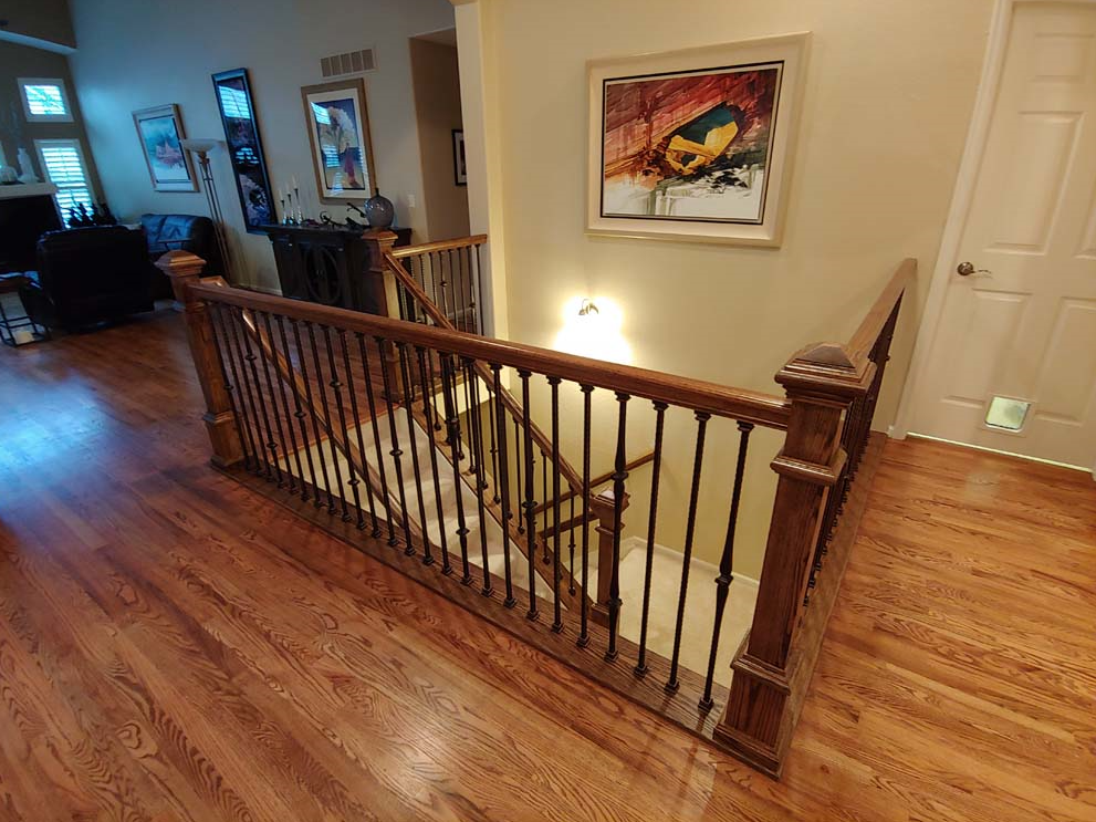 Wooden staircase with ornate railing leading down to a lower level. Artwork and a door are visible.