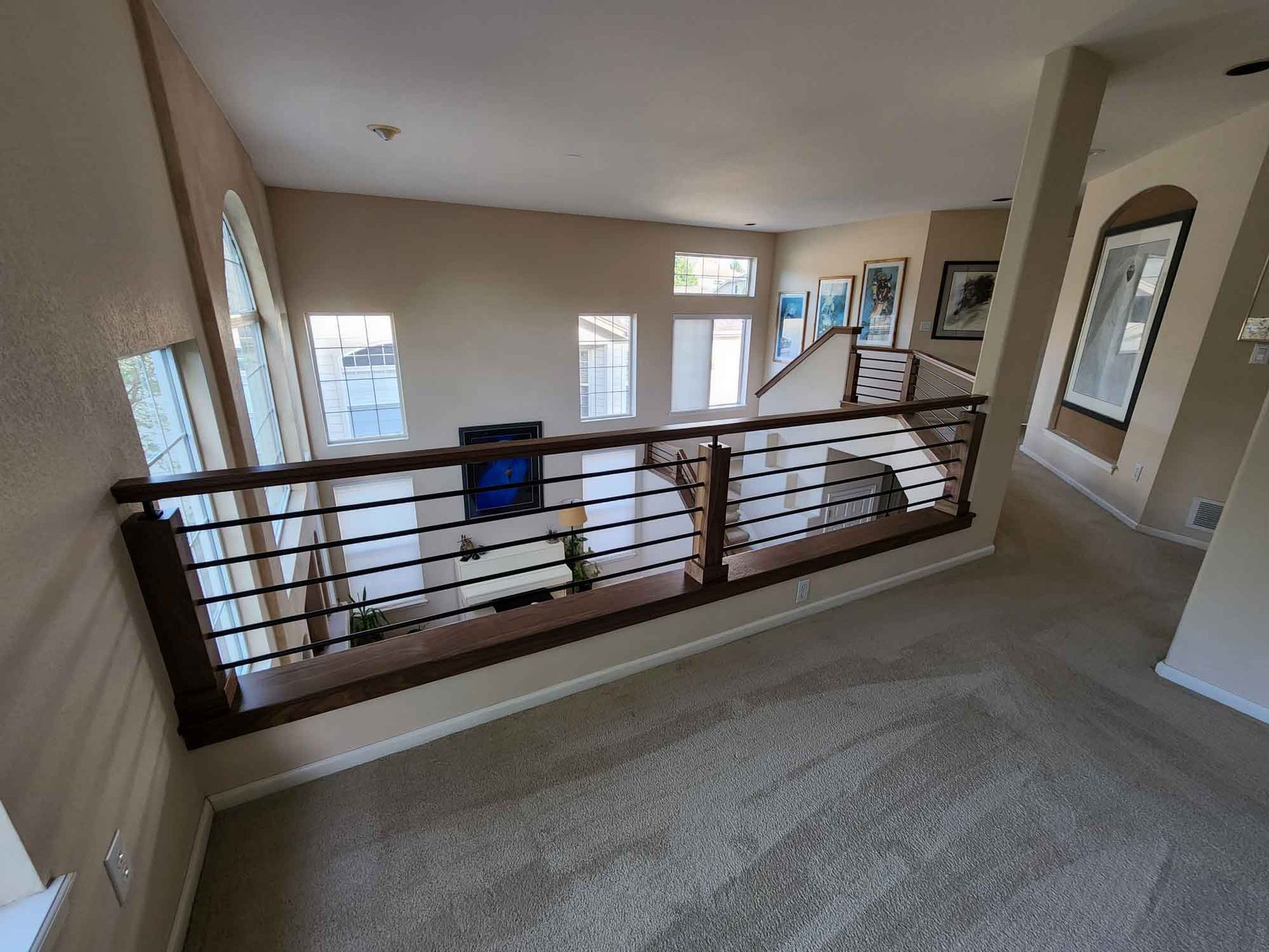 Interior view of a house with a carpeted upper level, railing, and windows.