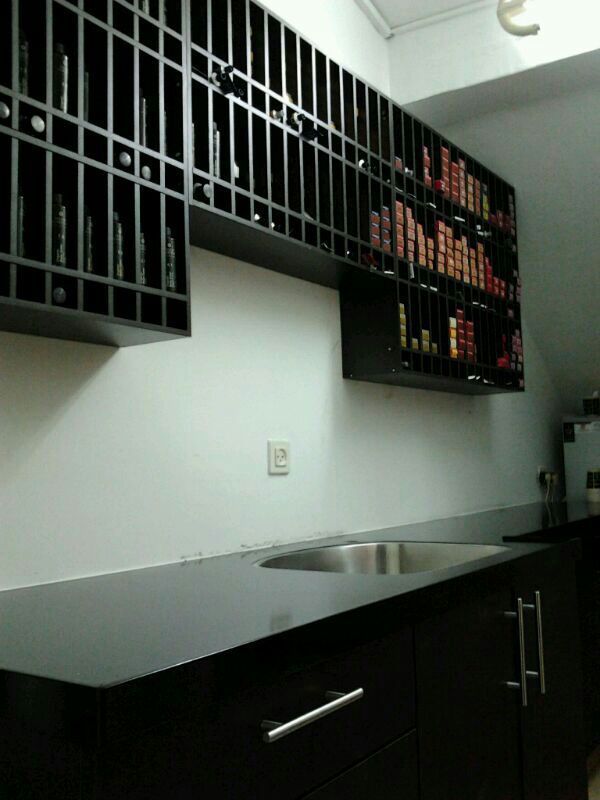 Dark wine rack above a dark countertop and cabinets with a stainless steel sink, set against a white wall.
