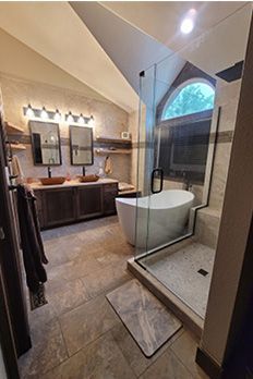 Bathroom with tub, shower, and double vanity. Beige tile, dark wood, and arched window.