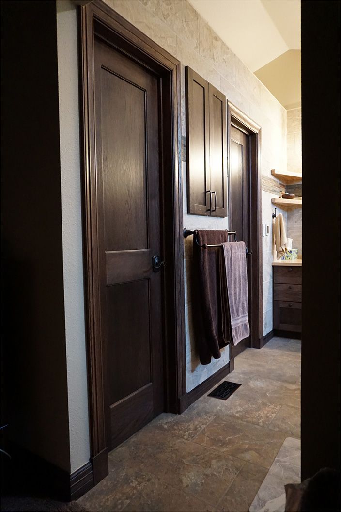 Dark wood doors and cabinets in a bathroom hallway with concrete floors. Towels hang on a rack.
