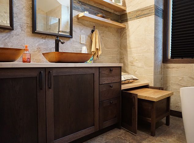 Bathroom vanity with wooden vessel sinks, dark cabinets, and a wooden bench.