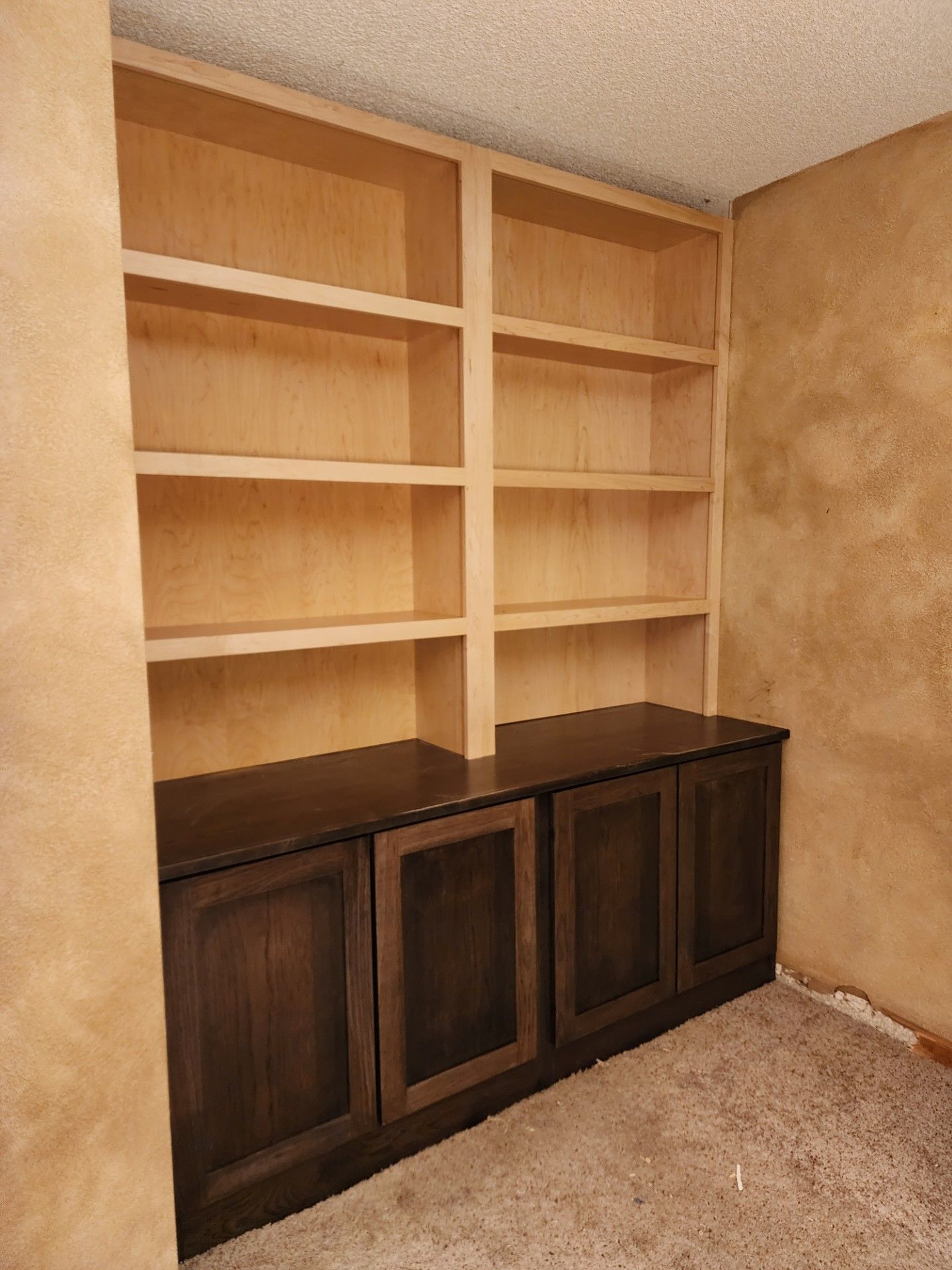 Built-in wooden bookcase with shelves above cabinets, stained brown, against tan walls and carpet.