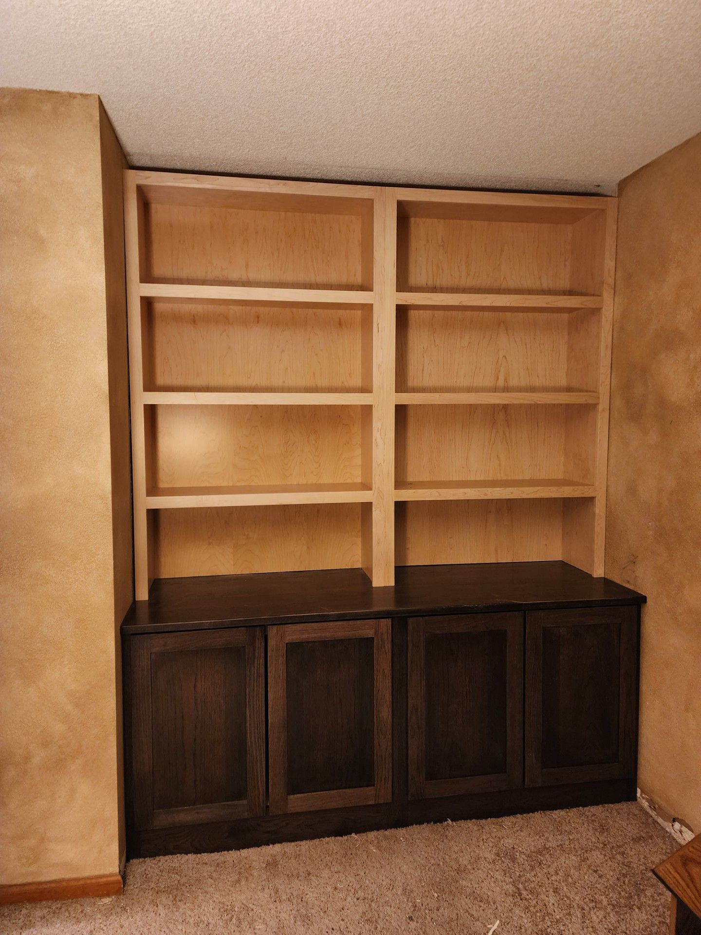 Built-in wooden bookcase with upper shelves and lower cabinets, finished with light wood and dark stain.