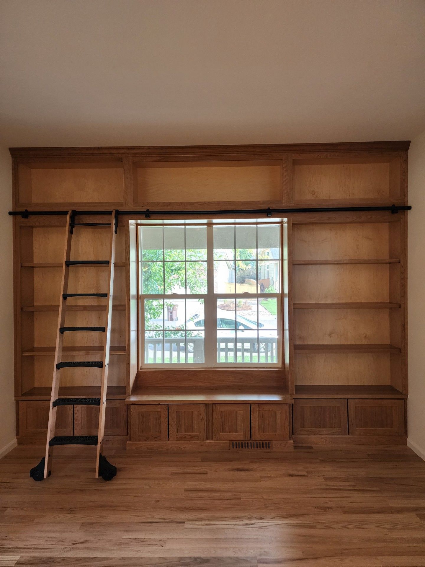 Wooden bookshelves framing a window with a reading nook, rolling ladder.