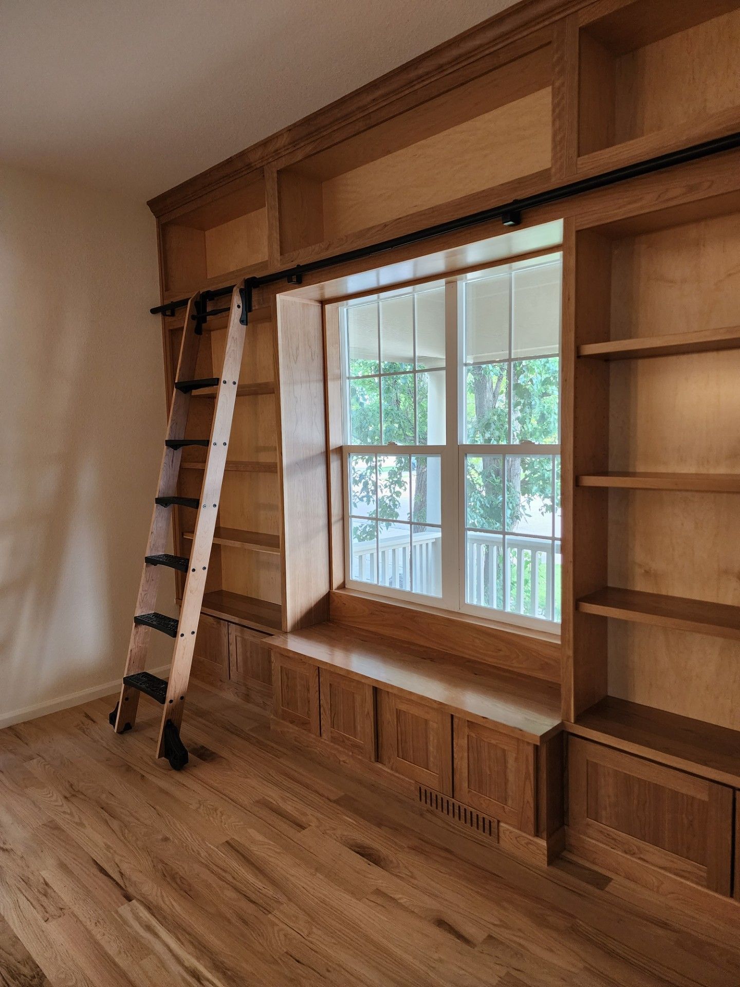 A room with wooden shelves and a ladder next to a window.