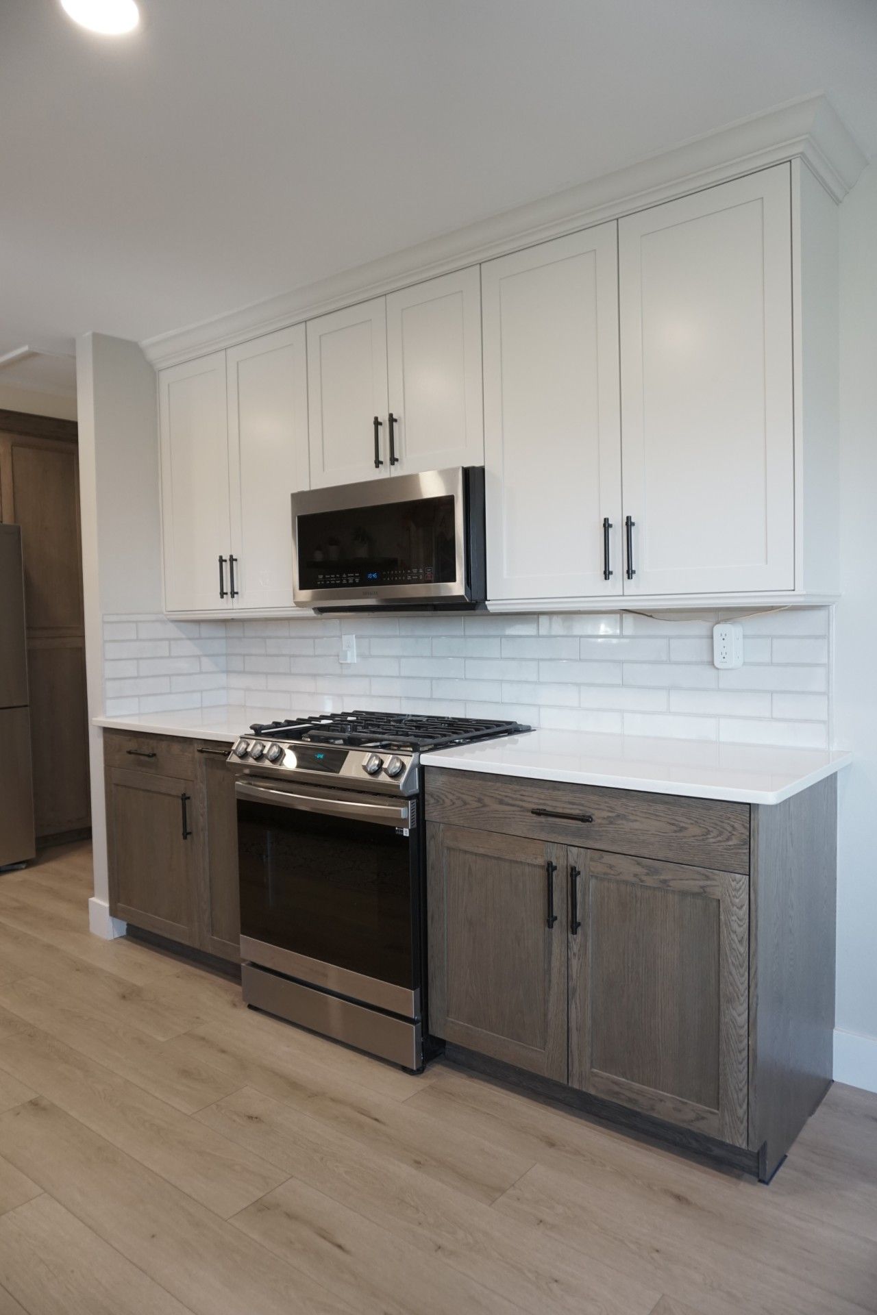Kitchen with white upper cabinets, gray lower cabinets, stainless steel appliances, and white tile backsplash.