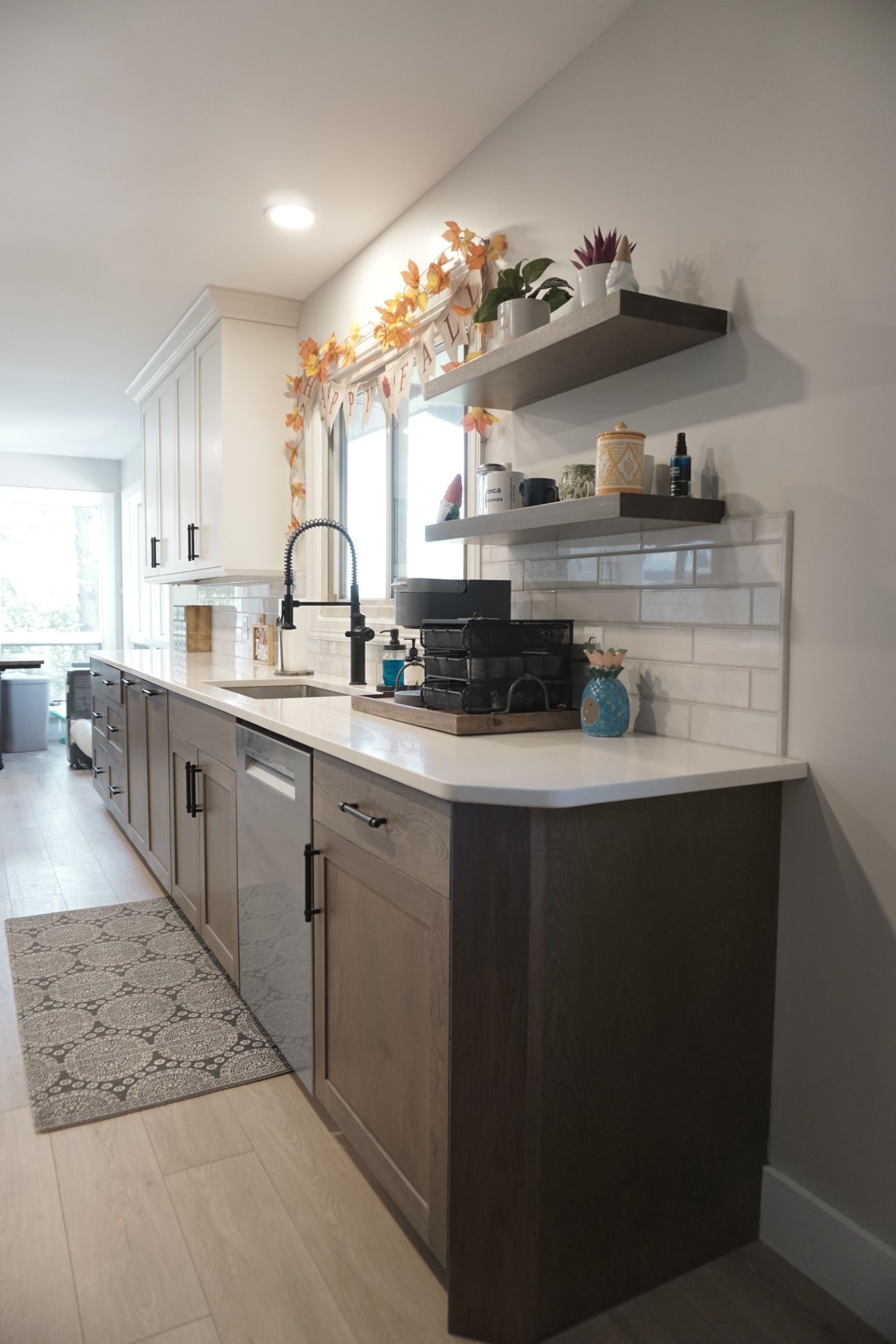 Modern kitchen with gray and brown cabinets, white countertops, and open shelving with decorations.