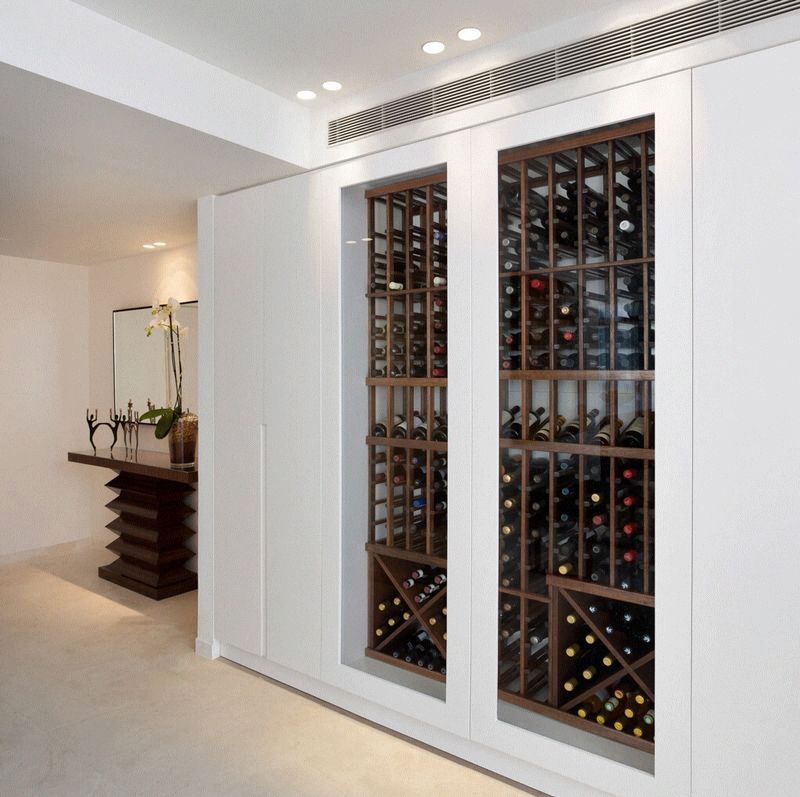 Built-in white wine storage with glass doors, displaying multiple bottles. The interior room is light and modern.