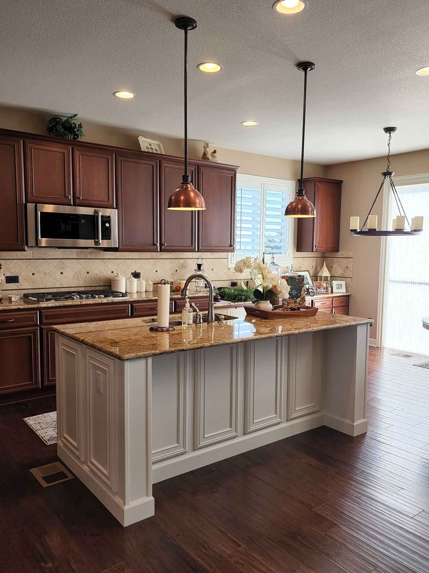 Kitchen with brown cabinets, island with granite countertop, pendant lights, and hardwood floors.