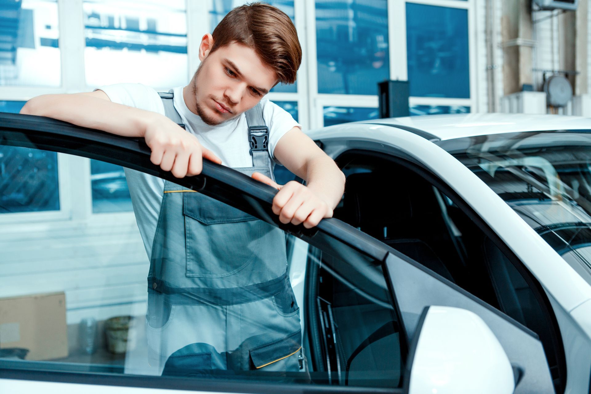 A man inspects a windshield in an auto factory, ensuring quality for an auto glass replacement shop.