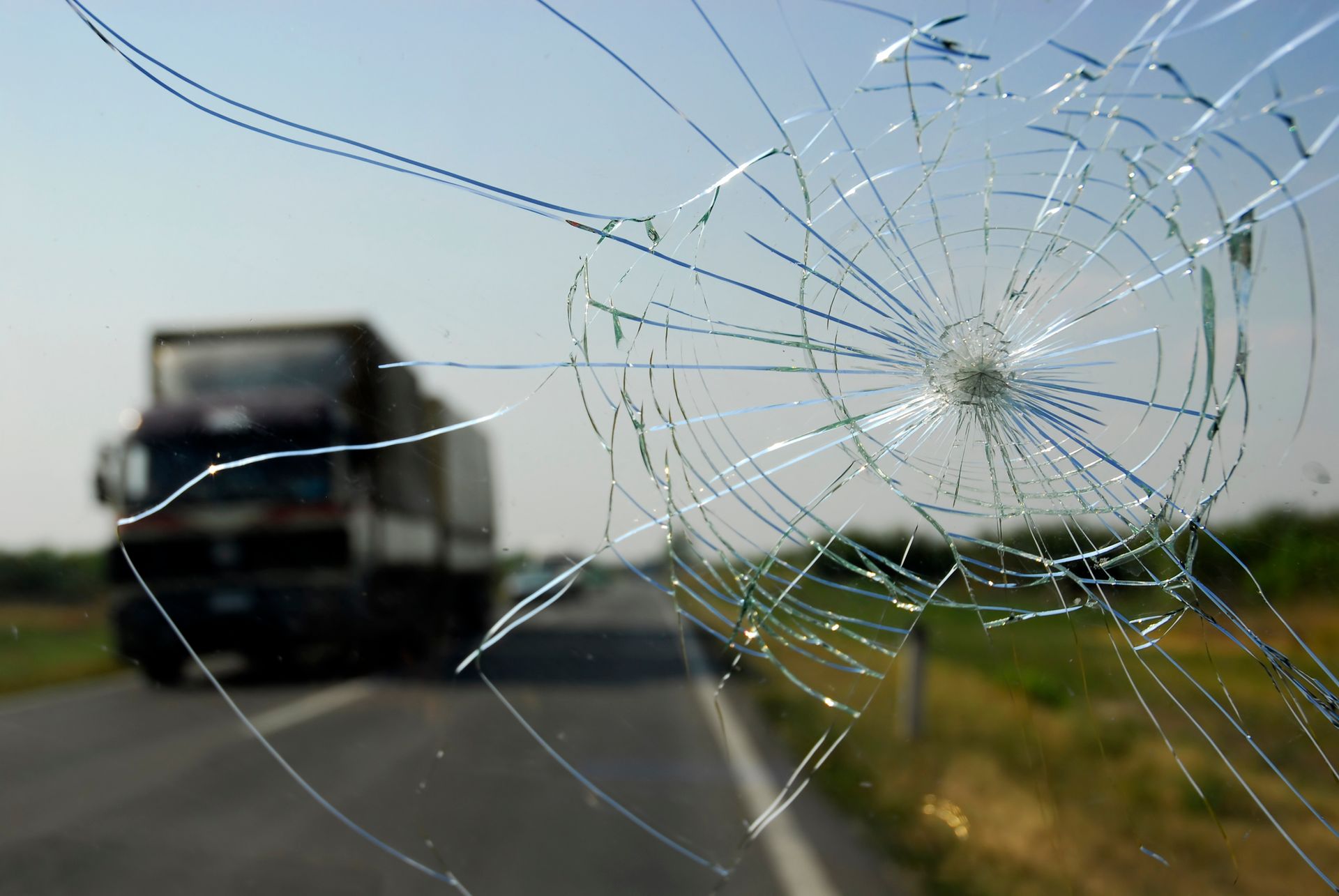 A broken windshield while driving on a road facing a truck on the other lane.