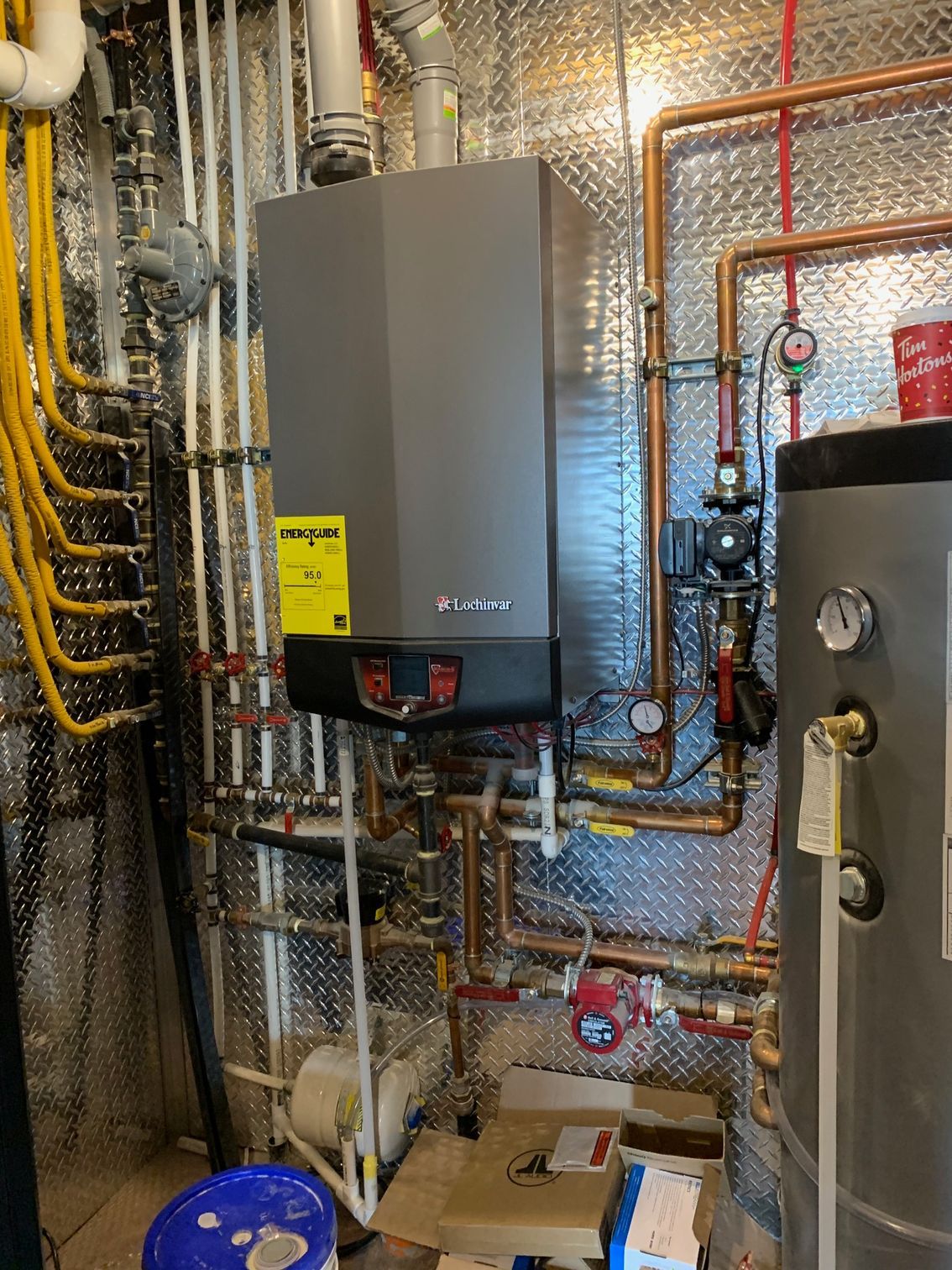 A boiler is sitting in a room surrounded by pipes.