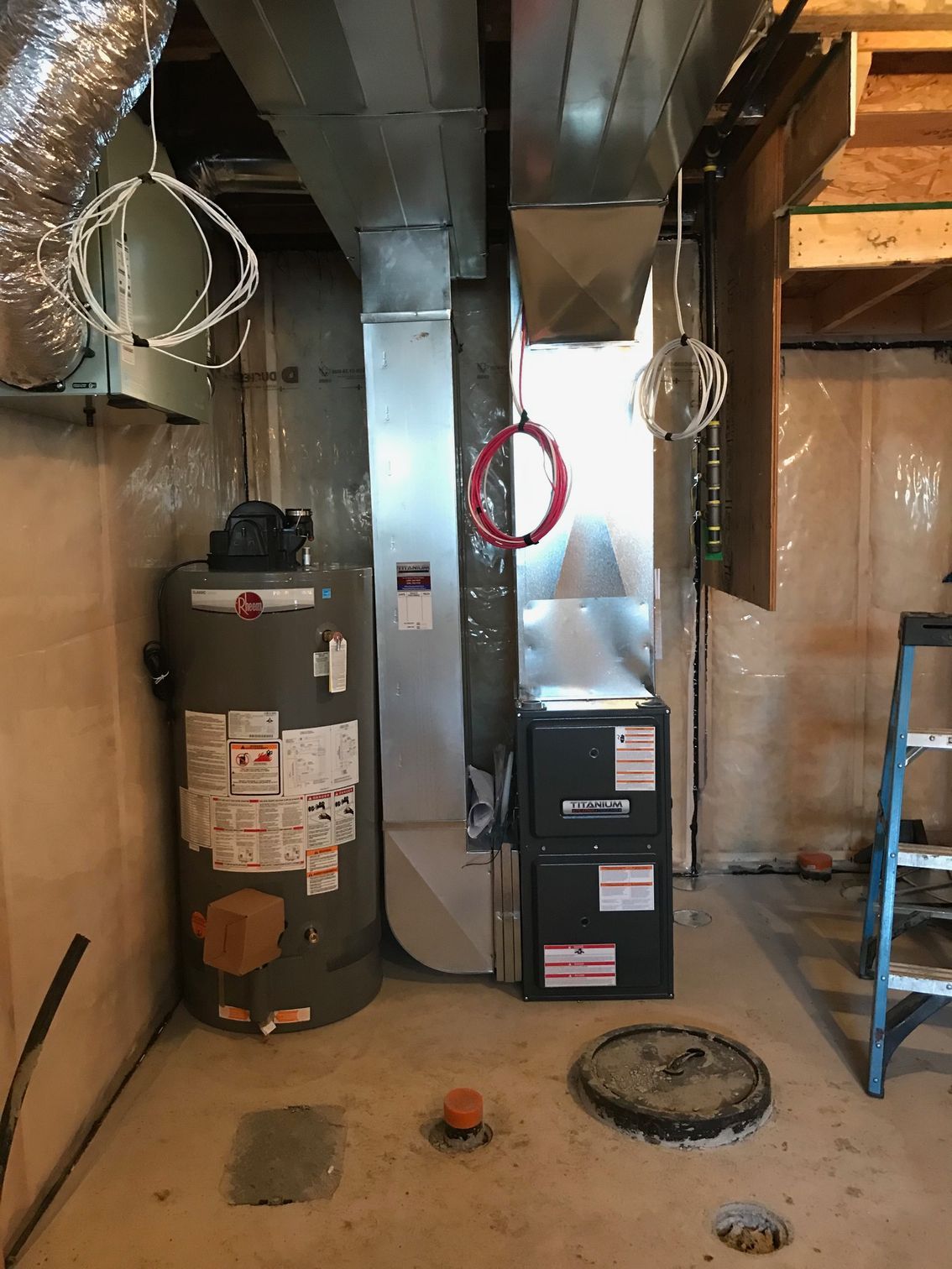 A basement with a water heater , air conditioner , and ladder.