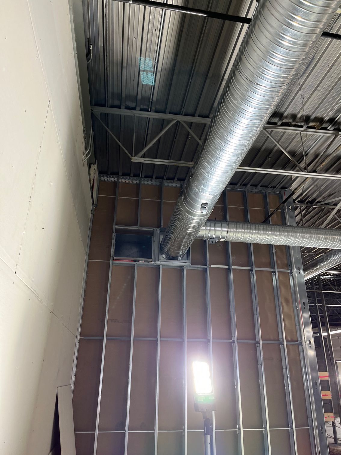A large metal pipe is hanging from the ceiling of a building under construction.