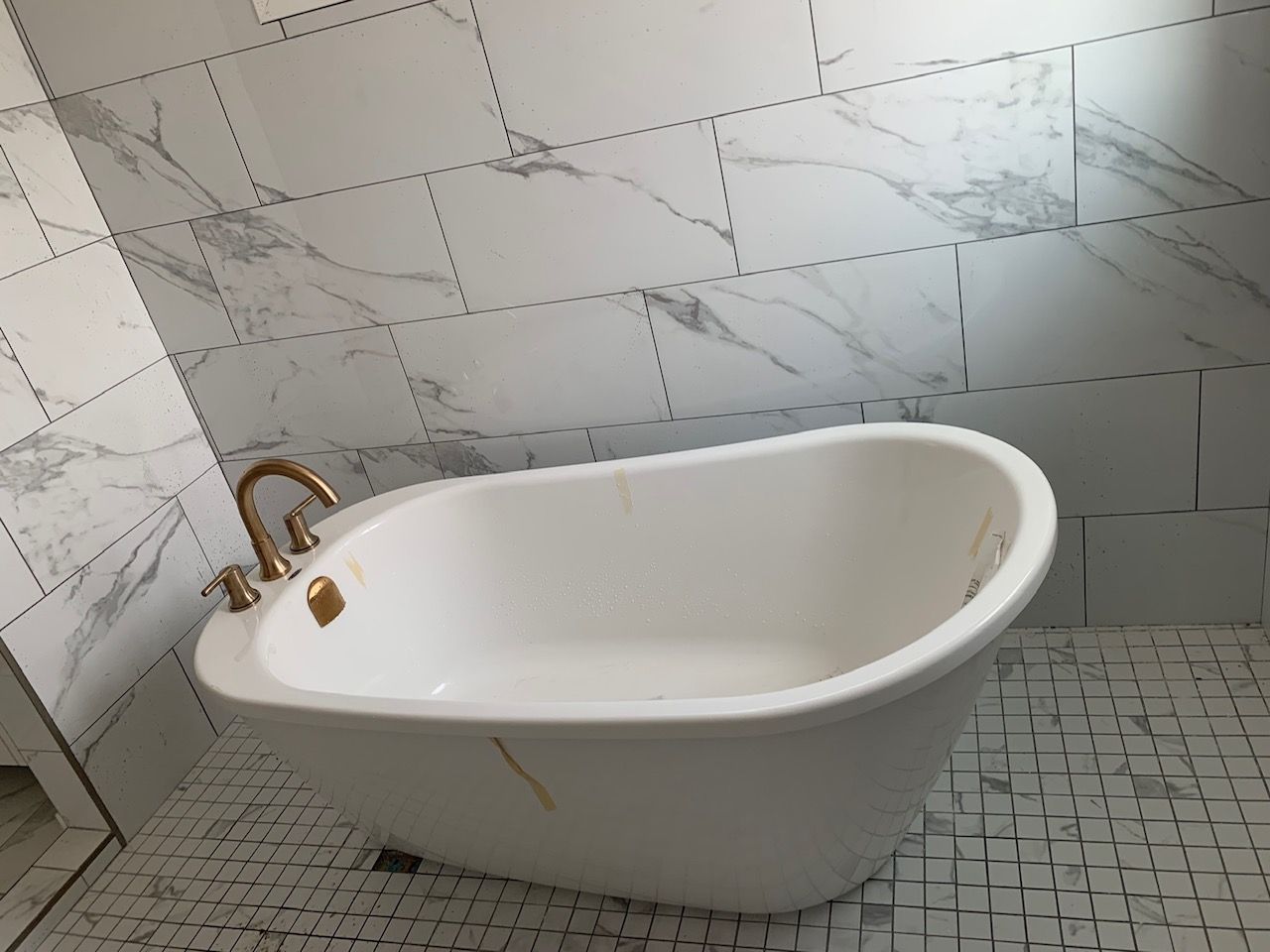 A white bathtub is sitting on a tiled floor in a bathroom.