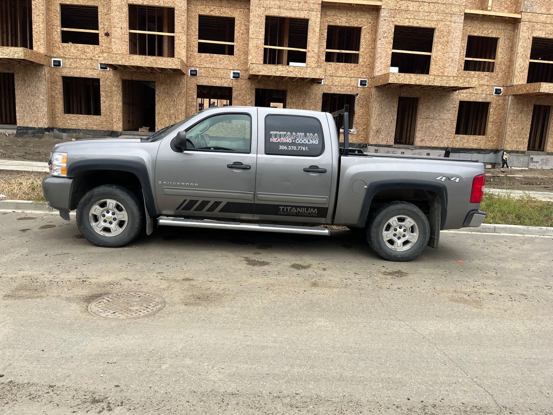 A gray truck is parked in front of a building under construction.